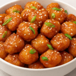 Honey Garlic Chicken Bites in a white bowl topped with sesame seeds and green onions