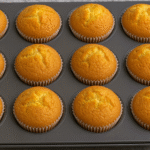 Fluffy bakery-style vanilla cupcakes in a muffin pan with golden tops, soft and moist, perfect for desserts and birthdays.